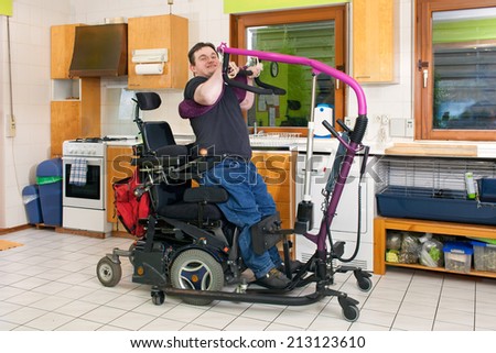 Spastic young man with infantile cerebral palsy caused by birth complications using a patient lift to maneuver himself into a multifunctional wheelchair for mobility