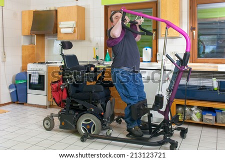 Young man with infantile cerebral palsy from birth complications using a patient lift to move from his bed to a multifunctional wheelchair