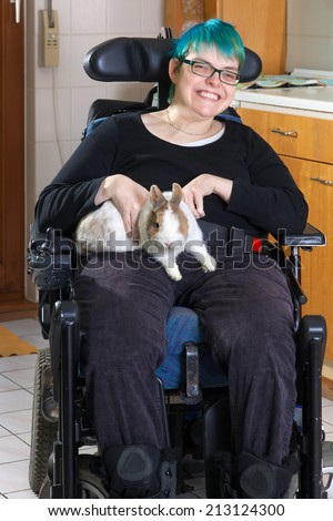 Young woman with infantile cerebral palsy due to birth complications confined to a multifunctional wheelchair caressing a pygmy rabbit as part of her therapy giving the camera a charming smile