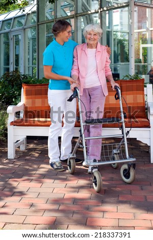 Loving daughter or care assistant helping her elderly mother as they enjoy a sunny day in the garden taking a walk with the use of a walking aid
