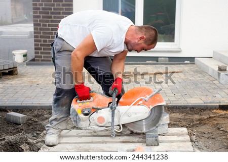 Worker with concrete saw in his hands, cutting concrete paving stones for creating a terrace.