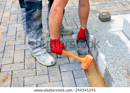 Close up of a worker places paving stones in front of a private house, using a rubber hammer for fixing the stones.