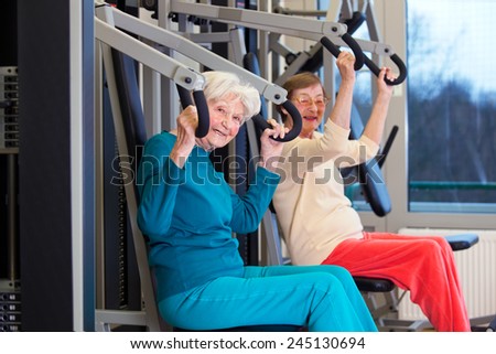 Modern Fit Elderly Ladies Working Out at the Fitness Gym Using Chest Press Equipment. Looking at the Camera.