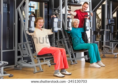 Smiling Elderly Women Working Out at the Fitness Gym with their Male Instructor, Looking at the Camera.