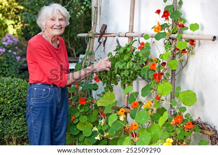 Smiling Old Woman Posing at her Flower Vines at her House Garden.