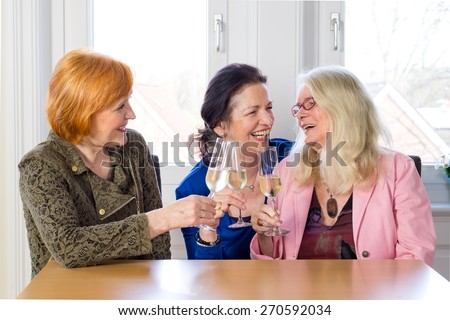 Three Happy Mom Friends Enjoying Glasses of Champagne at the Table Inside a Restaurant While Talking Funny Stories of their Lives.