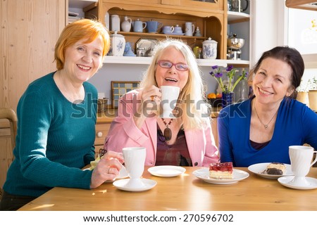 Three Smiling Mom Friends Sitting at the Wooden Table with Tasty Snacks and Looking at Camera.