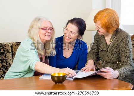 Three Happy Adult Women Friends Having Fun at the Living Room While Reading Magazine.