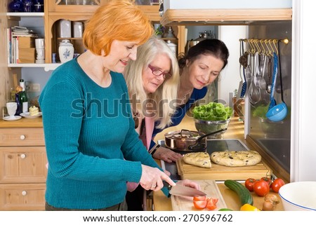 Curious Middle Age Moms Looking at their Smiling Friend Slicing Ingredients for their Dinner Recipe.