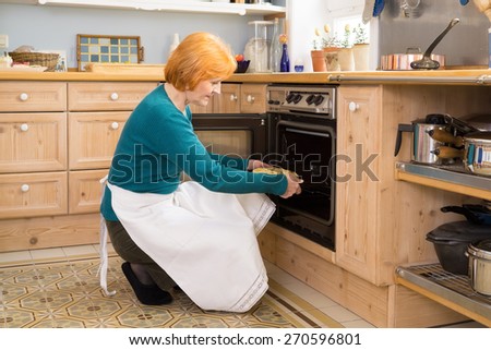 Blond Middle Age Woman With Apron Putting a Cake for Snacks in an Oven at the Home Kitchen.