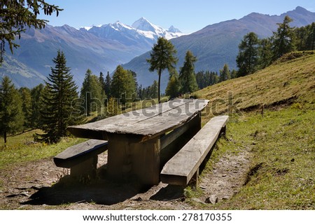 Scenic landscape with empty rustic picnic table and benches made of lumber on a grassy slope with coniferous trees and snow-capped Matterhorn mountain at the horizon, in Valais, Alps, Switzerland.