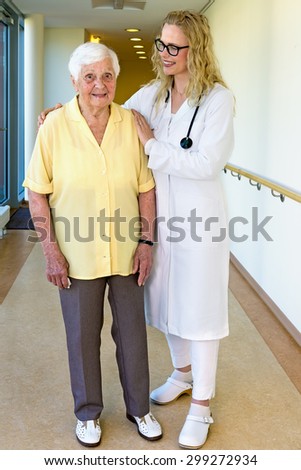 Kind Young Nurse in Uniform Assisting a Senior Woman with Special Needs While Walking at the Passage Way in the Nursing Home.