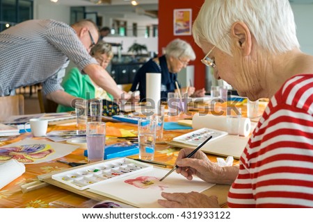 Woman in striped red and white shirt working on watercolor painting at table with other students in spacious studio