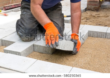 Hands of a builder laying new paving stones carefully placing one in position on a leveled and raked soil base