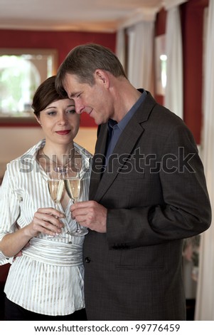 Attractive loving middle-aged couple standing close together clinking champagne glasses with tender expressions.