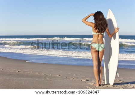 Rear view of sexy beautiful young woman surfer girl in bikini with white surfboard at a beach