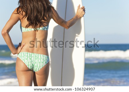 Rear view of a beautiful young woman surfer girl in bikini with white surfboard at a beach