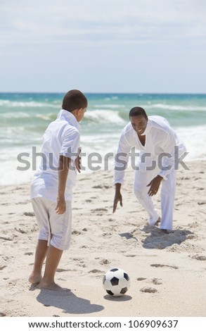A happy African American man and boy, father and son, playing football soccer on a beach