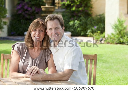 Attractive, successful, happy middle aged man and woman married couple in their thirties, sitting together outside in a garden sitting at a table.