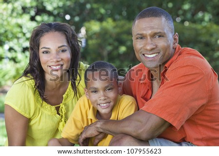 A happy, smiling African American family, mother father & son, man woman & child, outside in summer sunshine.