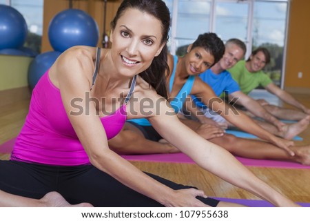 An interracial group of middle aged people, men and women, practicing yoga at a gym