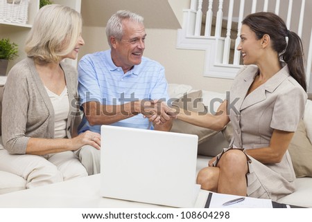 A saleswoman with laptop computer shaking hands with a senior couple at home