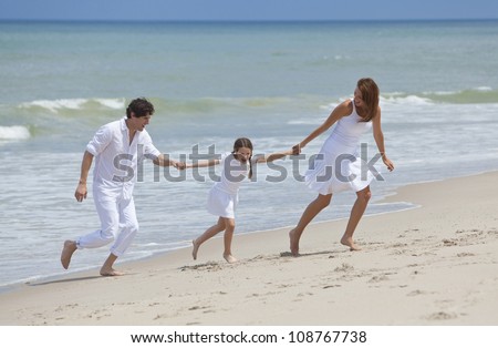 A happy family of mother, father and one child, a daughter, running holding hands and having fun in the sand of a sunny tropical beach