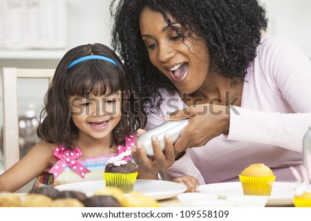 African American mother and mixed race daughter having fun frosting icing cup cakes
