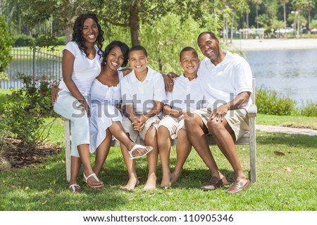 A happy black African American family of two parents and three children, two boys one girl, sitting together outside in white clothes