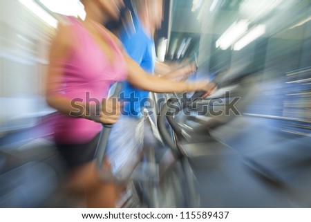 Motion blur zoom photograph of an interracial group of man and woman, running on equipment at a gym