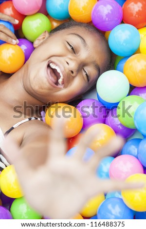 A young African American girl child having fun laughing playing with hundreds of colorful plastic balls