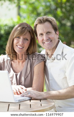 Attractive, successful and happy middle aged man and woman couple in their thirties, sitting together outside in a garden using a laptop computer.
