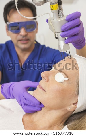 A cosmetic surgeon doctor giving fractional CO2 laser skin treatment to the face of a senior female woman patient