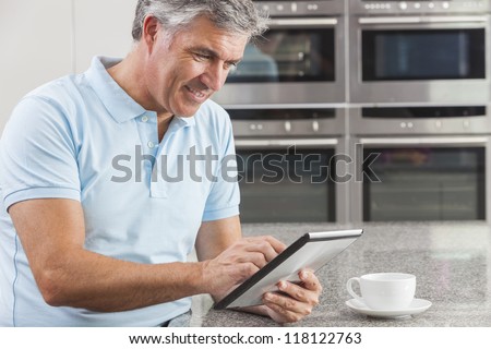 Middle aged man using tablet computer at home in the kitchen drinking coffee or tea