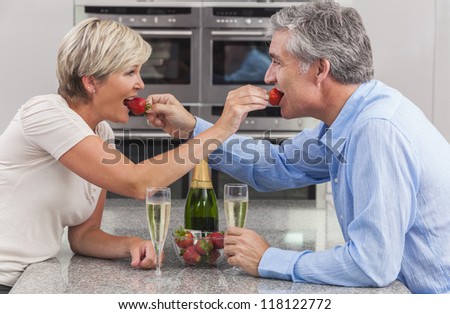 An attractive happy, smiling, romantic man and woman couple sharing strawberries and champagne in a kitchen