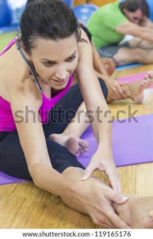 A woman and group of middle aged people, men and women, stretching & practicing yoga at a gym