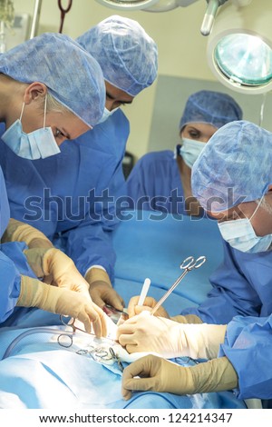 A team of interracial medical doctors male & female surgeons in surgery operating on a patient using different medical equipment instruments wearing scrubs and masks