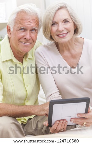 Happy senior man and woman couple sitting together at home on a sofa using a tablet computer