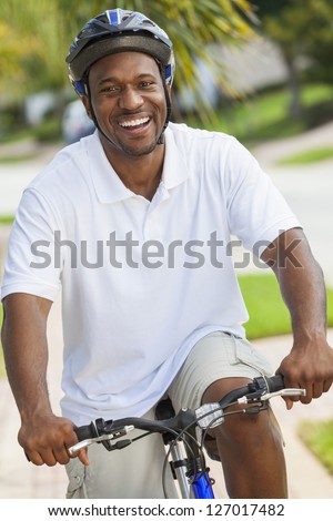 A happy African American man riding his bicycle outside wearing shorts, helmet and polo t-shirt
