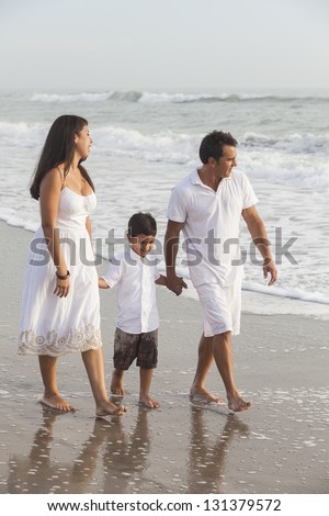 A happy family of mother, father and child, boy sons, holding hands & walking in the sand of a beach