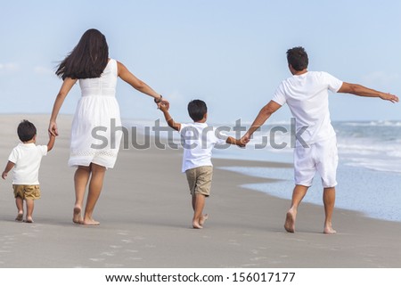 Rear view of happy family of mother, father and two children, boy sons, walking holding hands and having fun in the sand on a sunny beach
