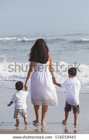 Family of mother parent & two boy son children, walking and holding hands in the waves of a beach