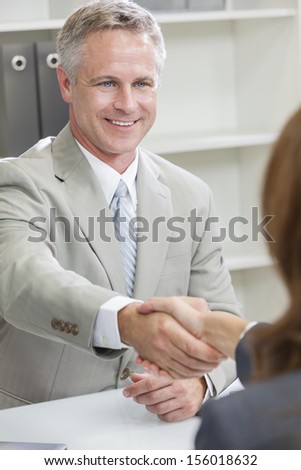 Man or businessman shaking hands handshake in office meeting with female colleague