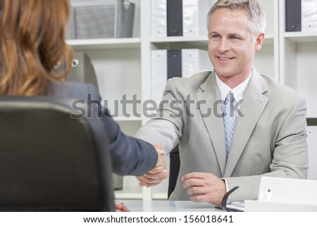 Man or businessman shaking hands handshake in office meeting with female colleague