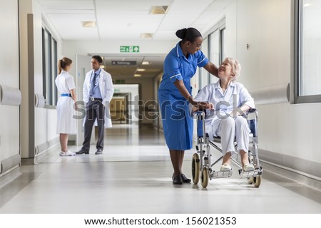 Senior female woman patient in wheelchair sitting in hospital corridor with African American female nurse and doctor