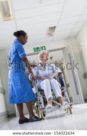 Senior female woman patient in wheelchair sitting in hospital corridor with black African American female nurse