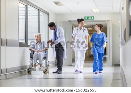 Doctors & nurse in hospital corridor with senior female patient in wheel chair with male Asian doctor