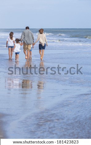 Rear view of family mother, father, daughter, parents and female girl children walking in the sea on a beach