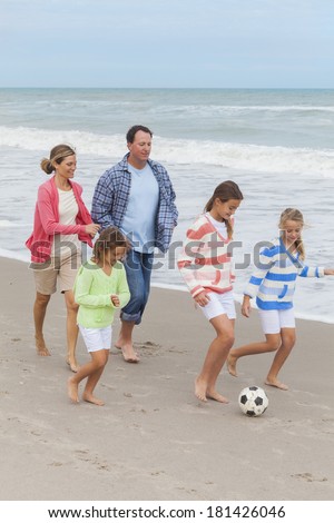 Family mother, father, daughter, parents and female girl children having fun playing football or soccer on a beach