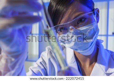 A Chinese Asian Oriental female medical or scientific researcher or doctor using looking at a test tube of liquid in a blue laboratory.